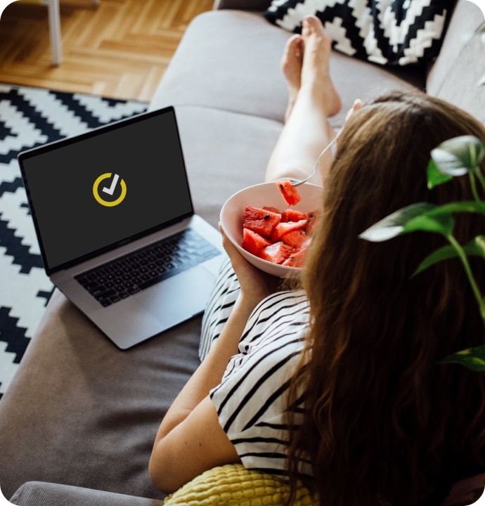 소파에서 수박을 먹으면서 노트북에서 Norton 360 AntiVirus Plus를 실행하는 여성